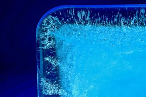 Ice cube on blue background and hard white light Stockfoto's