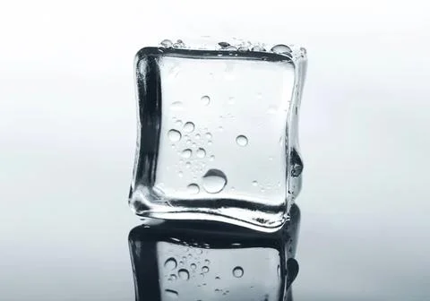 Ice cube with bubbles melting on a reflective surface Stock Photos