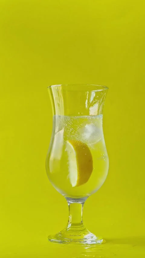 Ice cube falling into a cocktail glass with sparkling mineral water,lemon slice. Stock Footage 338182523