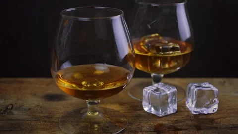 Ice cube falling into cognac \ whiskey glass, golden color strong spirit alcohol Stock Footage 135583427