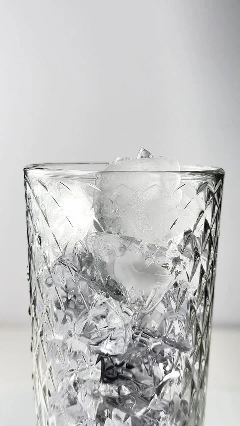 Ice cube falling into cut glass tumbler on clean white studio background fo.. Stock Footage 338403217