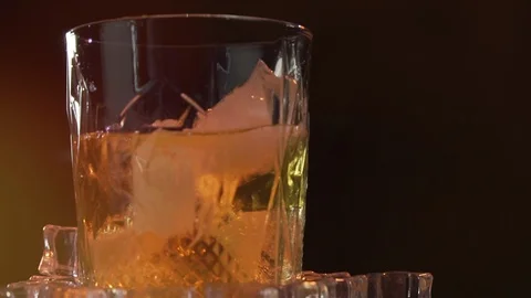 Ice cube falls and melts in a glass of malt whiskey Video stock 124577447