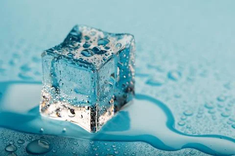 Ice cube with water drops on a blue background. The ice is melting. Stock Photos