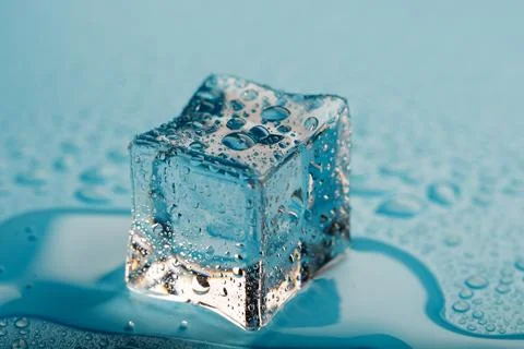 Ice cube with water drops on a blue background. The ice is melting. Stock Photos
