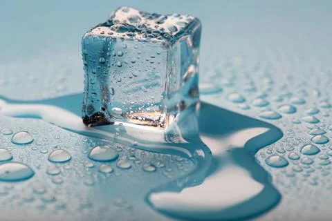 Ice cube with water drops on a blue background. The ice is melting. Stock Photos