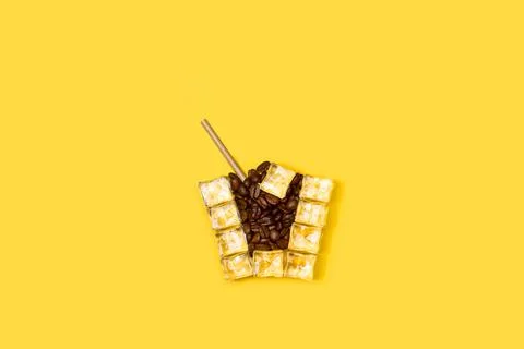 Ice cubes and coffee beans drinking glass shaped on a yellow background Foto stock