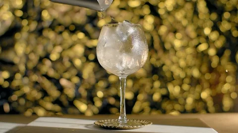 Ice cubes are being dropped to the cocktail glass in slow motion on the golden Stock Footage 166962221