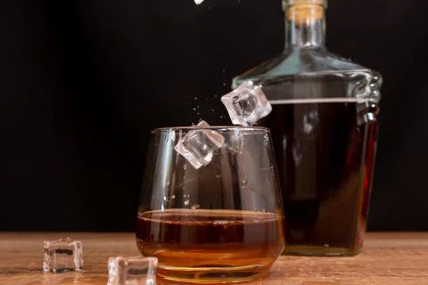 Ice cubes are slowly falling into a glass filled with whiskey Stock Photos
