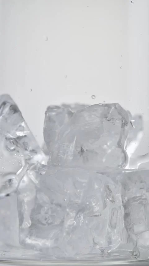 Ice cubes fall into clear glass in macro view, creating cold texture for Stock Footage 346066267