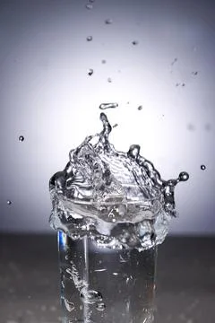 Ice cubes fall into the glass and splash with dynamic water Stock Photos