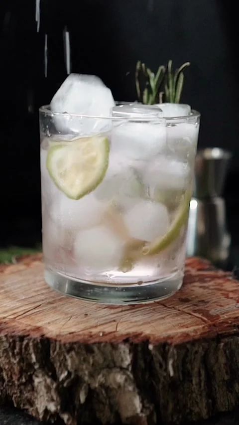 Ice cubes fall into a glass with lime and rosemary and topped with soda. The Stock Footage 279915489