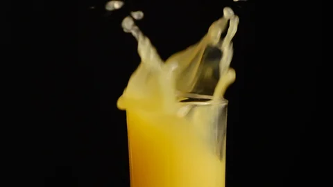 Ice cubes fall in glass of orange fruit juice or lemonade on black background. Stock Footage 123066923
