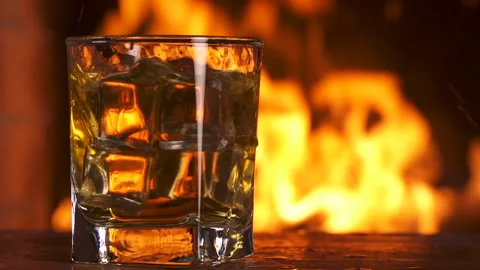 Ice cubes fall into a glass Whiskey. Fireplace With a Flame. Alcoholic Drink. Stock Footage 138599883