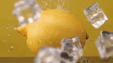 Ice cubes fall on the lemon. Slow motion. Yellow background. Macro mode. Freshne Stock Footage 144334375