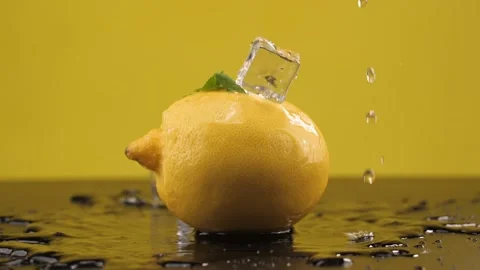 Ice cubes fall on the lemon. Slow motion. Yellow background. Macro mode. Freshne Stock Footage 144334409