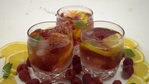 Ice cubes fall in three glasses of lemonade from raspberries and citrus fruits Stock Footage 247641926