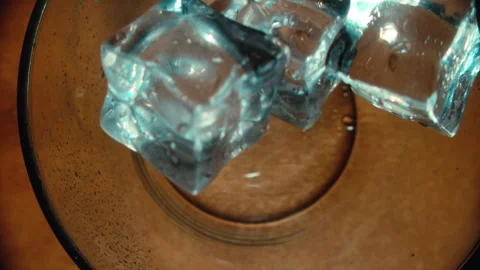 Ice Cubes Falling into a Clear Glass Bowl on a Wooden Surface Vidéo 331098883