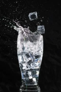 Ice Cubes falling into drinking glass with a splash Stock Photos
