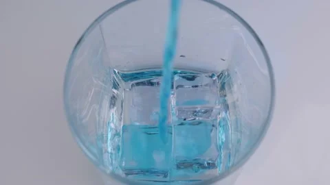 Ice cubes falling into an empty glass. Pouring blue drink into a glass Stock Footage 130823809