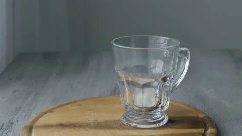 Ice Cubes falling into an empty transparent Glass on wooden desk Stock Footage 170605287