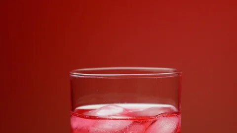 Ice cubes falling in the glass with red soda water, making splash and bubbles Stock Footage 109664699