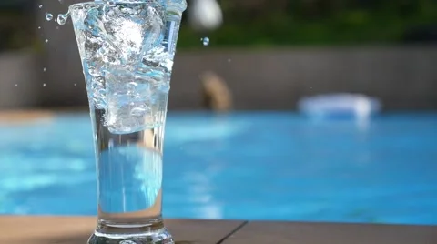 Ice Cubes Falling in Glass of Water near Swimming Pool. Slow Motion. Stock Footage 45697164