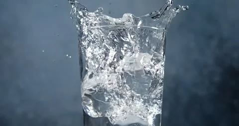 Ice cubes falling into a glass of water with splash in slow motion Stock Footage 345367792