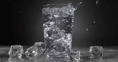 Ice cubes falling into a glass of water with splash in slow motion Stock Footage 345451161
