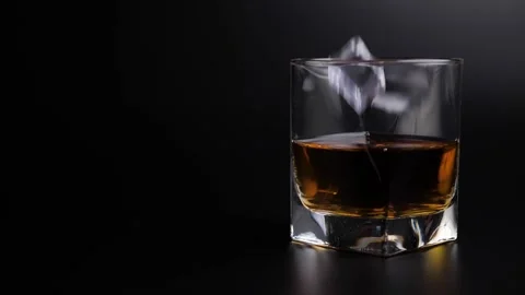 Ice cubes falling into glass of whiskey over black background Stock Footage 132324613