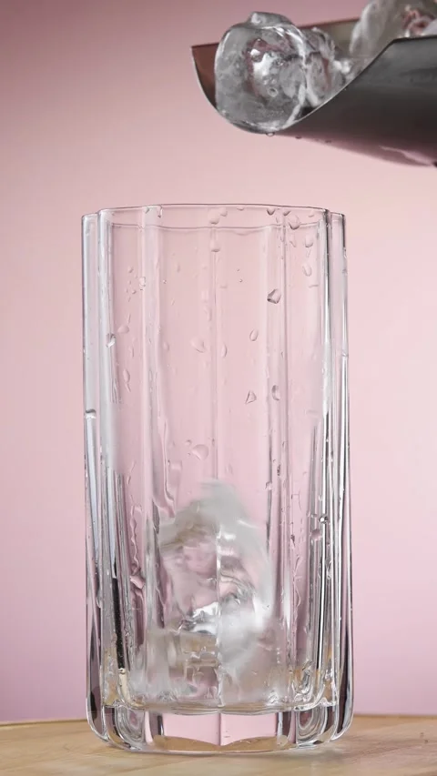 Ice cubes fill rotating tall glass on pink background during preparation of Stockbeeldmateriaal 346064157