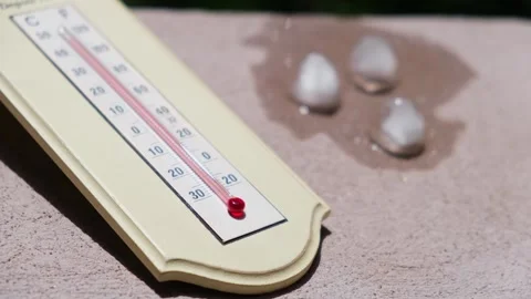 Ice cubes melting in direct sun next to a home thermometer Vídeo Stock 247216661