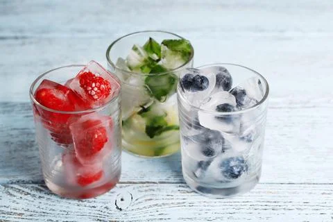 Ice cubes with mint leaves, raspberry and blueberry in glasses, on color wo.. Stock Photos
