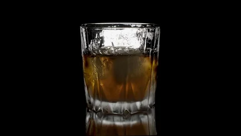 Ice cubes rotating and melts in a glass of whiskey. Isolated on black Stock-Footage 125402507