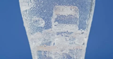 Ice cubes rotating in a glass with crystal clear water on a blue background Vídeos de archivo 246147772