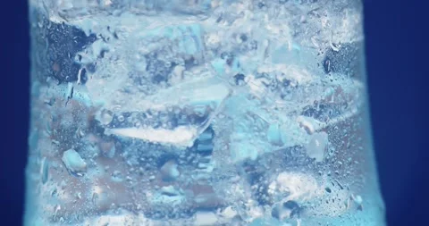 Ice cubes rotating in a glass with crystal clear water on a blue background Stock Footage 246148010
