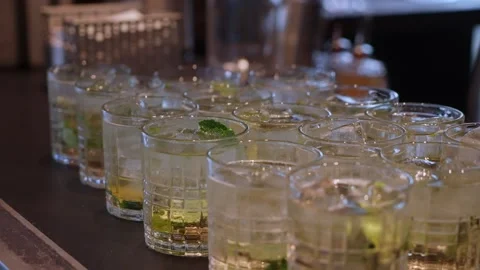 Ice Cubes Shimmer Beneath Vibrant Light, Busy Bartender Arranges Beverages With 스톡 동영상 323776920