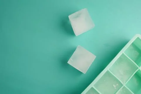 Ice cubes on a turquoise surface with an ice tray nearby Stock Photos