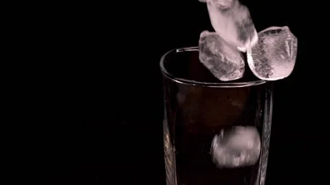 Ice fall into a clear, empty single malt glass. The glass is on a black stand. Stock Footage 150669397