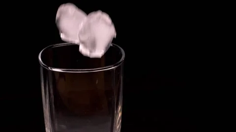 Ice fall into a clear, empty single malt glass. The glass is on a black stand. Stock Footage 150669412