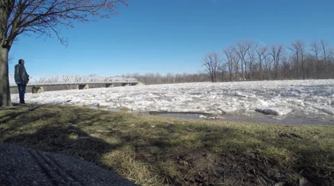 Ice Flowing down river towards bridge as pedestrian watches Stock Footage 49747369