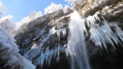 Ice formations forming under a waterfall falling from the side of a rocky cliff Stock Footage 118972086