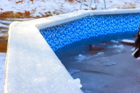 Ice forms along edge of swimming pool on chilly winter morning in quiet backyard Stock Photos