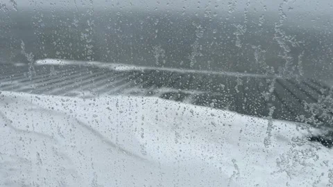 Ice on glass window as winter storm blows snow over roof and out to sea Stock Footage 327675067