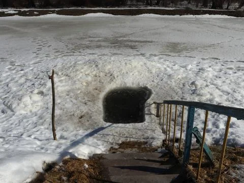 Ice hole by the river during winter season with steps leading down to water and Stock-Fotos
