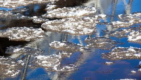 Ice patterns are visible on a body of water surrounded by reflections and cle Stock Photos