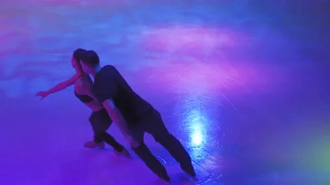 Ice skaters couple slides on empty rink in color light Stock-Footage 137456001