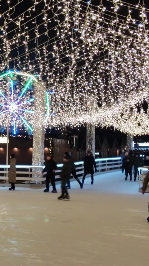 Ice skating under festive lights with a ferris wheel in the background Stock-Footage 312326554