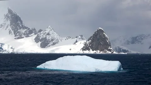Iceberg drifting across frame mountains Antarctica, 4K Stock Footage 332372907