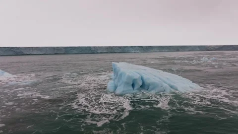 Iceberg floating in the Arctic ocean with massive ice shelf in the horizon Stock Footage 291622319