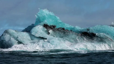 Iceberg rolling up on itself, cloudy and blue sky, Arctic Ocean Vidéo 92111810